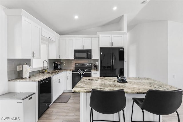 kitchen with lofted ceiling, white cabinetry, a sink, light stone countertops, and black appliances