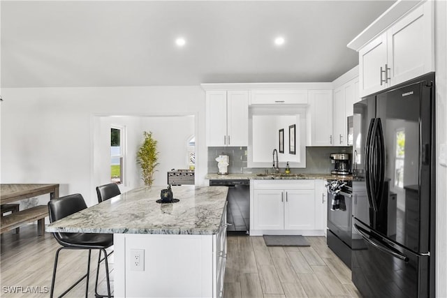 kitchen with decorative backsplash, a breakfast bar, black appliances, white cabinetry, and a sink