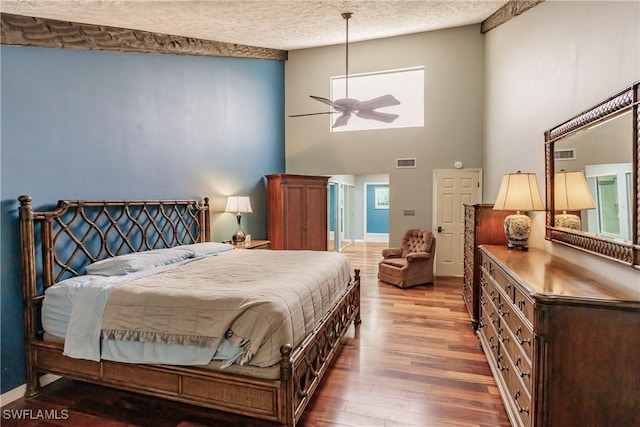 bedroom featuring visible vents, a towering ceiling, a textured ceiling, wood finished floors, and baseboards