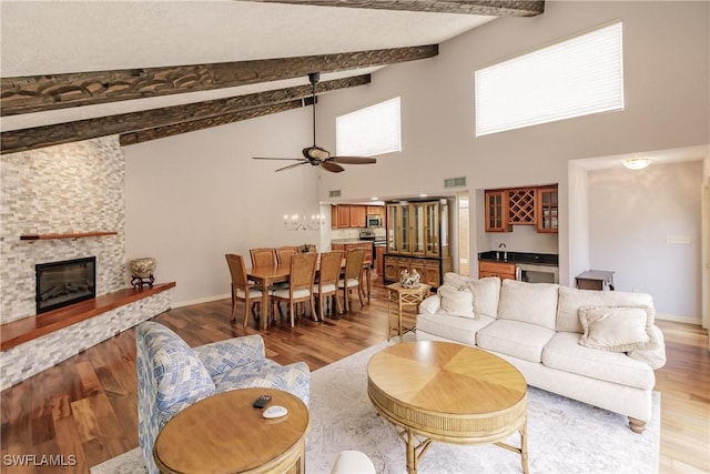 living room with light wood-style flooring, a fireplace, visible vents, beam ceiling, and indoor wet bar