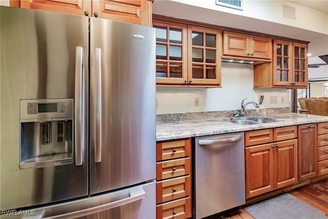 kitchen with visible vents, brown cabinetry, light stone counters, stainless steel appliances, and a sink