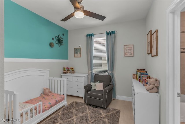 bedroom featuring a nursery area, ceiling fan, baseboards, and light wood-style flooring