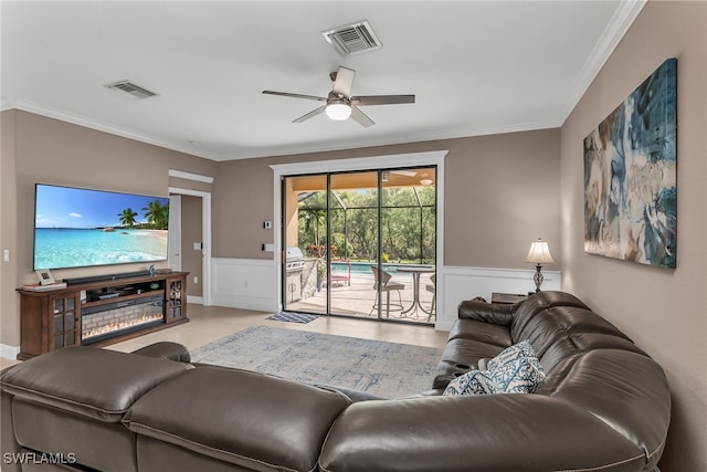 living room featuring ornamental molding, a wainscoted wall, visible vents, and ceiling fan