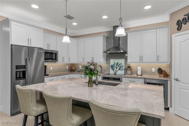 kitchen with wall chimney exhaust hood, appliances with stainless steel finishes, a breakfast bar area, and crown molding