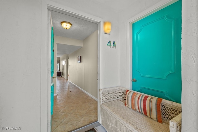 hall featuring a textured ceiling, tile patterned flooring, and baseboards