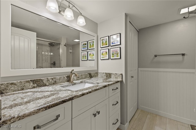 full bathroom featuring a stall shower, vanity, wood finished floors, and wainscoting