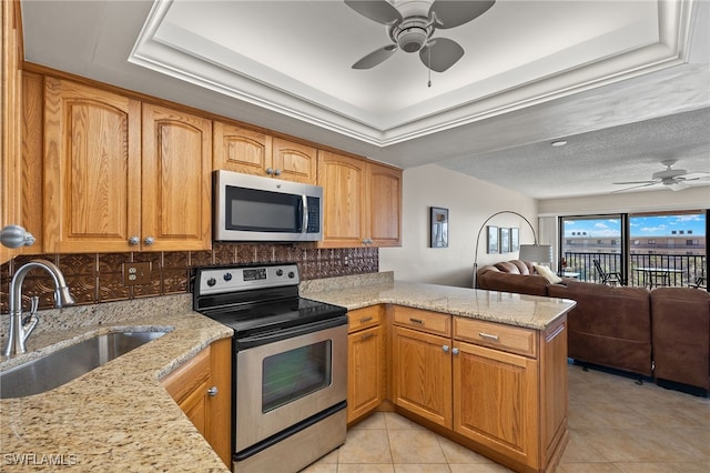 kitchen with open floor plan, a peninsula, a tray ceiling, stainless steel appliances, and a sink