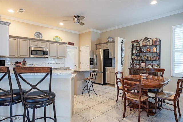 kitchen featuring visible vents, decorative backsplash, appliances with stainless steel finishes, a breakfast bar area, and gray cabinets