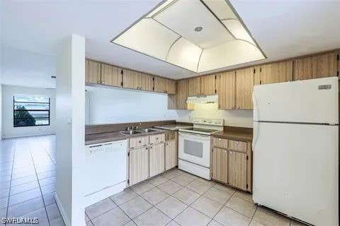 kitchen featuring white appliances, dark countertops, under cabinet range hood, a sink, and light tile patterned flooring