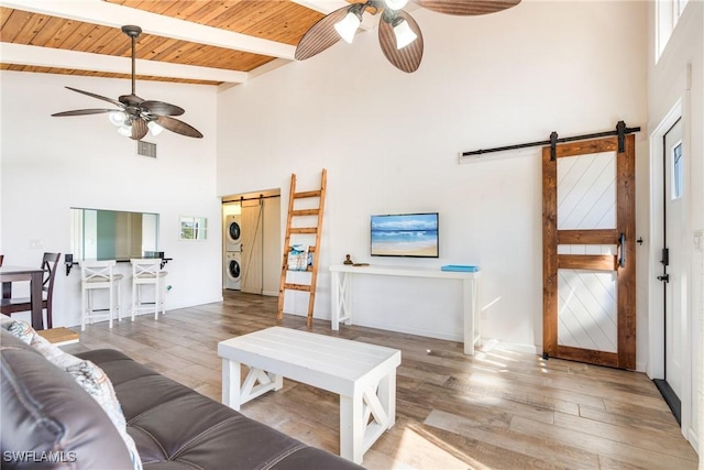 living room featuring stacked washer and dryer, a ceiling fan, wooden ceiling, and a barn door