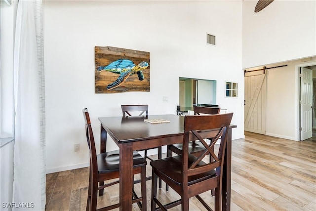 dining room with light wood-type flooring, a barn door, visible vents, and baseboards