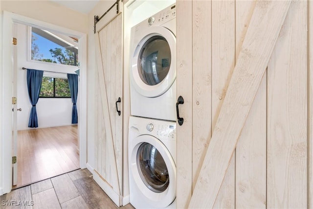 laundry area with laundry area, a barn door, stacked washer and clothes dryer, and light wood-style floors