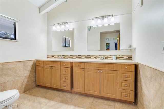 full bath with toilet, wainscoting, vanity, and tile walls