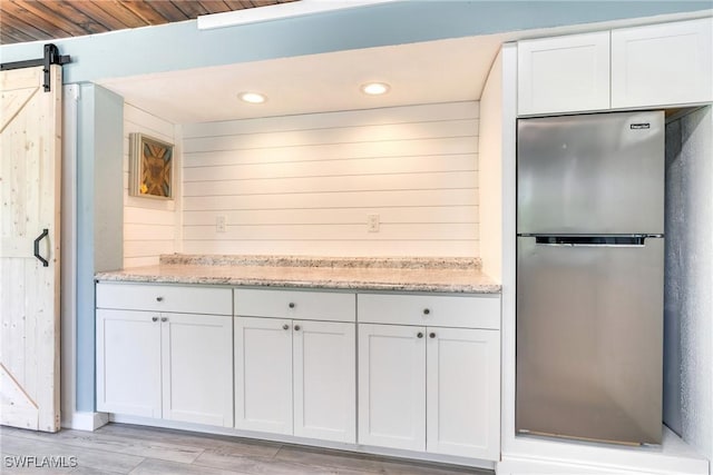 kitchen with a barn door, light stone counters, freestanding refrigerator, light wood-type flooring, and white cabinetry