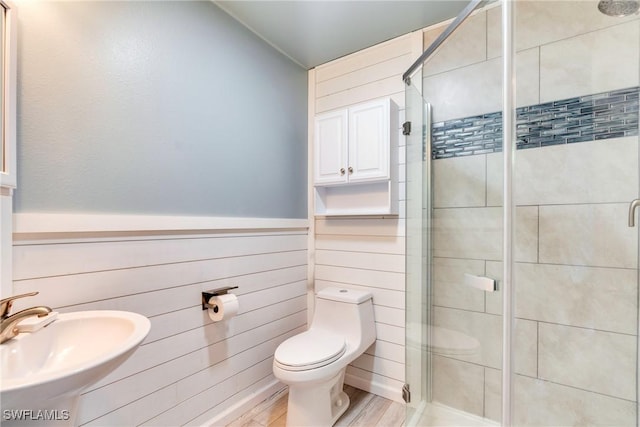 bathroom featuring toilet, a wainscoted wall, wood walls, a shower stall, and a sink