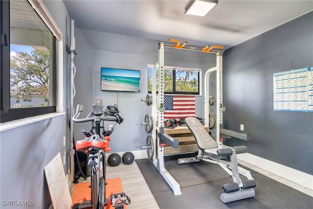 exercise room with baseboards, wood finished floors, and a healthy amount of sunlight