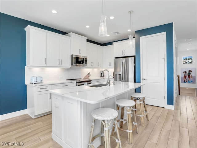 kitchen featuring wood finish floors, a sink, visible vents, appliances with stainless steel finishes, and backsplash