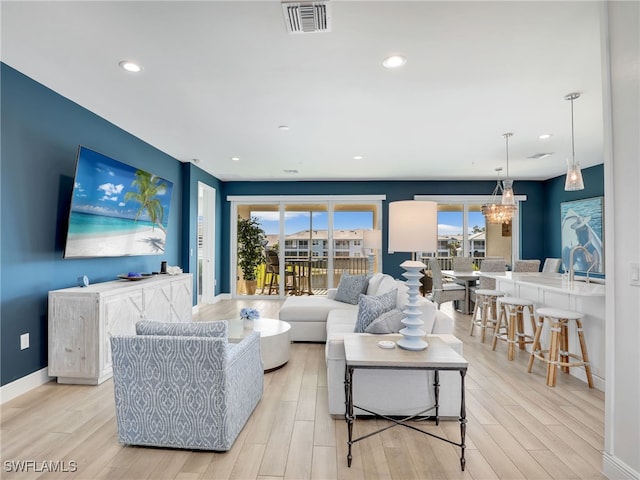 living area featuring light wood finished floors, baseboards, visible vents, and an inviting chandelier