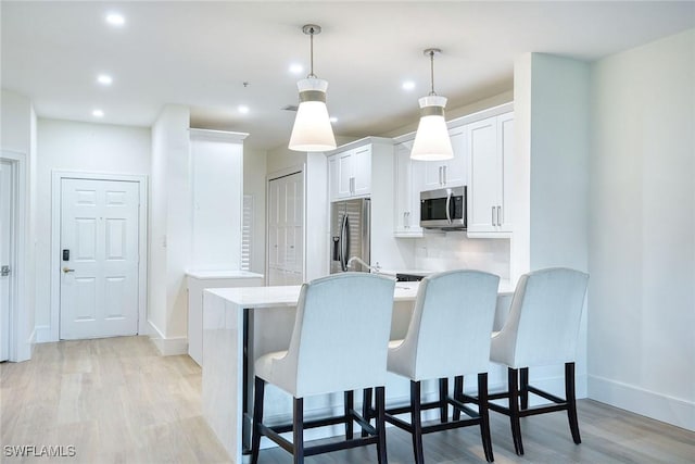 kitchen featuring light wood finished floors, light countertops, appliances with stainless steel finishes, white cabinetry, and a peninsula