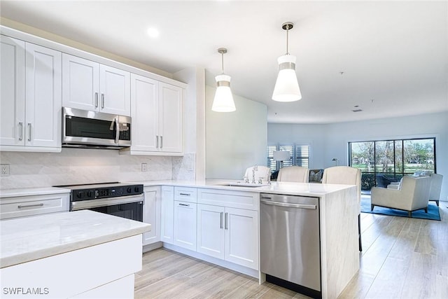 kitchen featuring appliances with stainless steel finishes, a sink, light wood-style flooring, and a peninsula