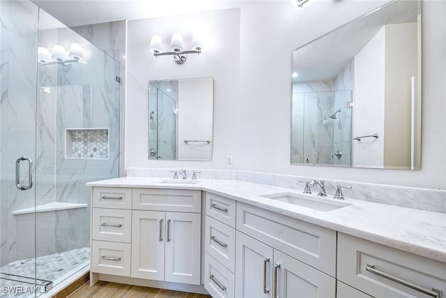 full bathroom featuring double vanity, wood finished floors, a sink, and a marble finish shower