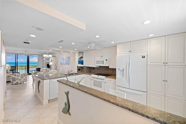 kitchen with light tile patterned floors, a peninsula, white appliances, a sink, and white cabinetry