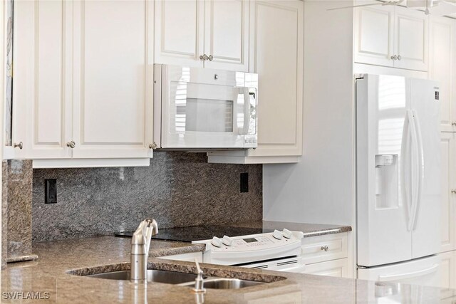 kitchen featuring light stone counters, backsplash, white cabinets, a sink, and white appliances