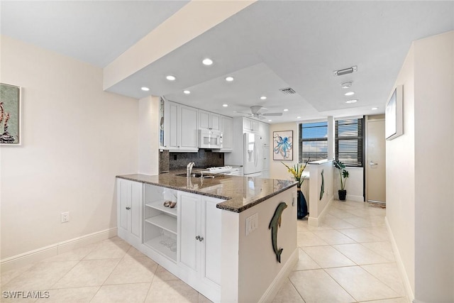 kitchen featuring white appliances, light tile patterned floors, visible vents, a peninsula, and backsplash