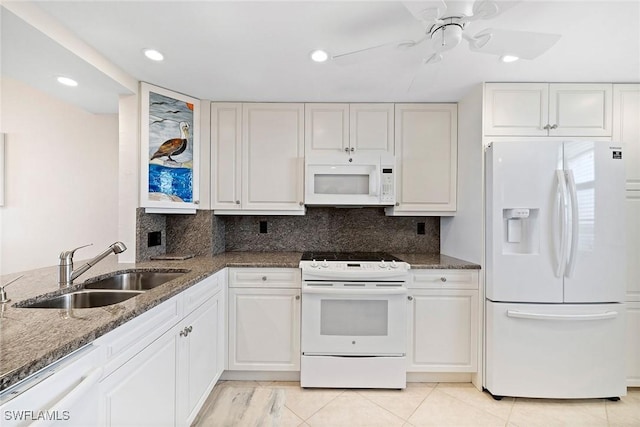 kitchen featuring dark stone counters, white appliances, a sink, and a ceiling fan