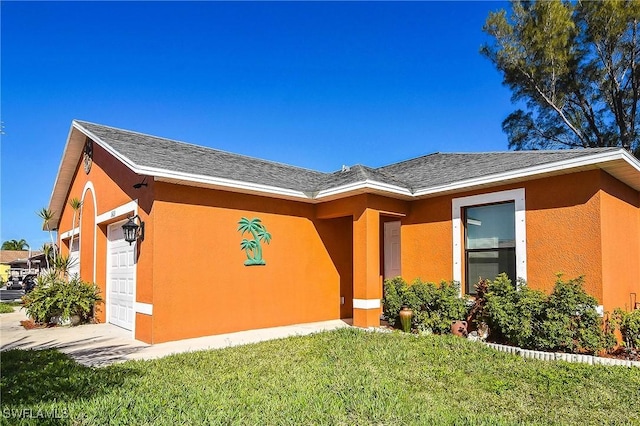 entrance to property with a garage, roof with shingles, a yard, and stucco siding