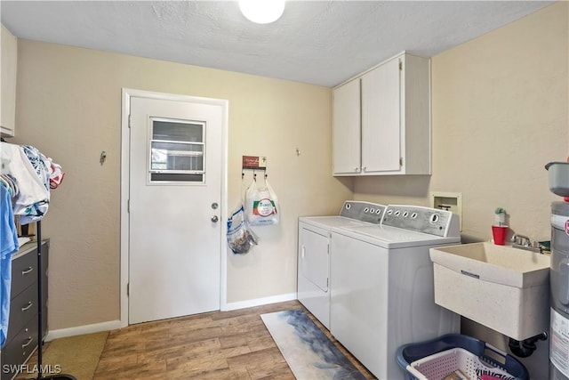 washroom featuring cabinet space, baseboards, light wood-style floors, separate washer and dryer, and a sink