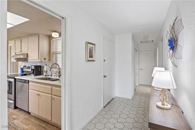 kitchen with light brown cabinets, under cabinet range hood, stove, a sink, and dishwasher