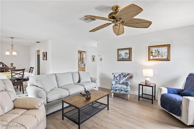 living area with ceiling fan with notable chandelier, baseboards, visible vents, and light wood-style floors