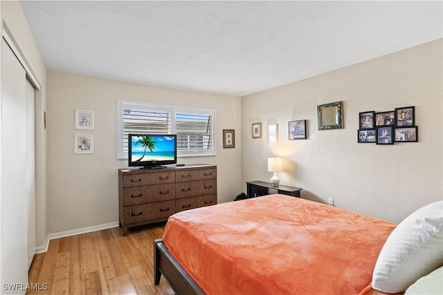 bedroom featuring light wood finished floors, baseboards, and a closet