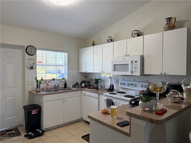 kitchen featuring light tile patterned flooring, vaulted ceiling, a sink, white appliances, and a peninsula