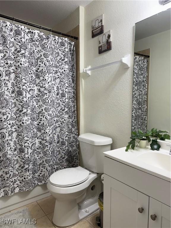 bathroom with toilet, a textured wall, tile patterned flooring, and vanity