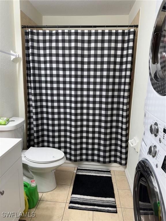 bathroom featuring curtained shower, tile patterned flooring, toilet, stacked washer and dryer, and vanity