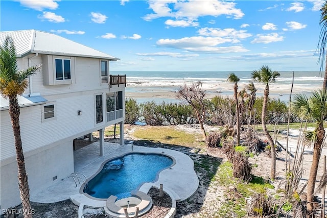 pool with a patio area, a water view, and a beach view