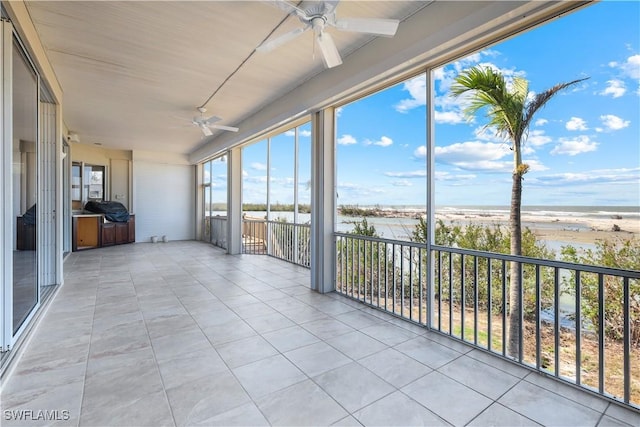 unfurnished sunroom with plenty of natural light, a beach view, a ceiling fan, and a water view