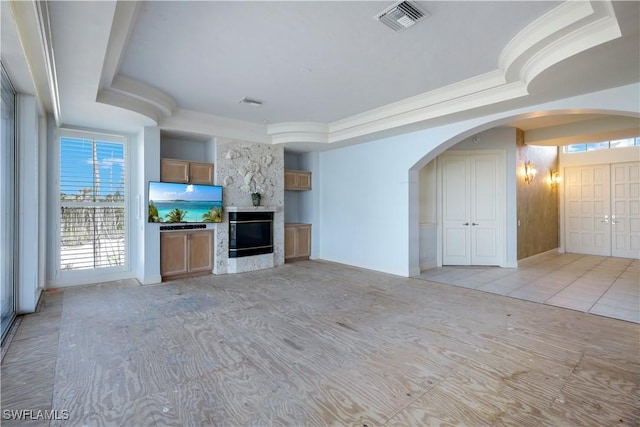 unfurnished living room with arched walkways, visible vents, a high end fireplace, a raised ceiling, and crown molding