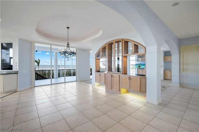 unfurnished dining area featuring an inviting chandelier, baseboards, a tray ceiling, and light tile patterned flooring