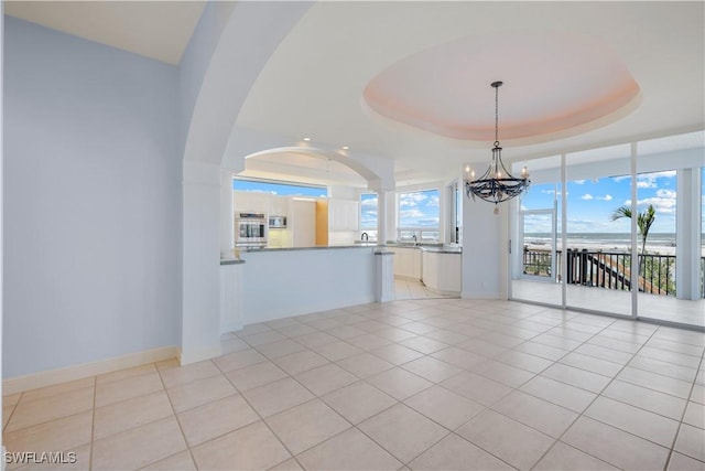 spare room featuring a notable chandelier, light tile patterned flooring, a raised ceiling, and baseboards