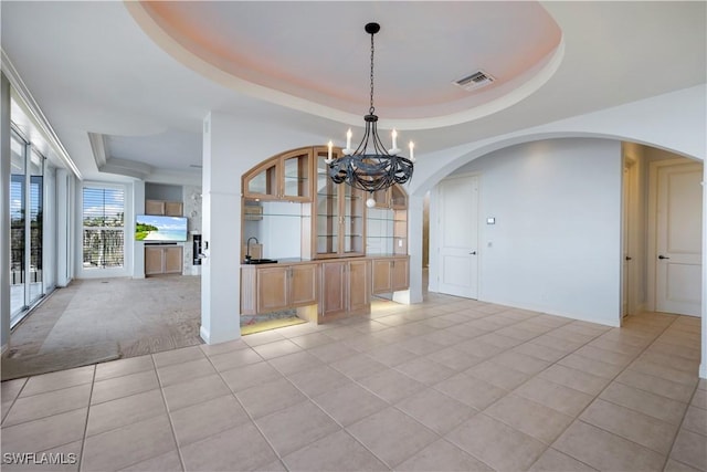 unfurnished dining area with light tile patterned floors, a sink, visible vents, a tray ceiling, and an inviting chandelier