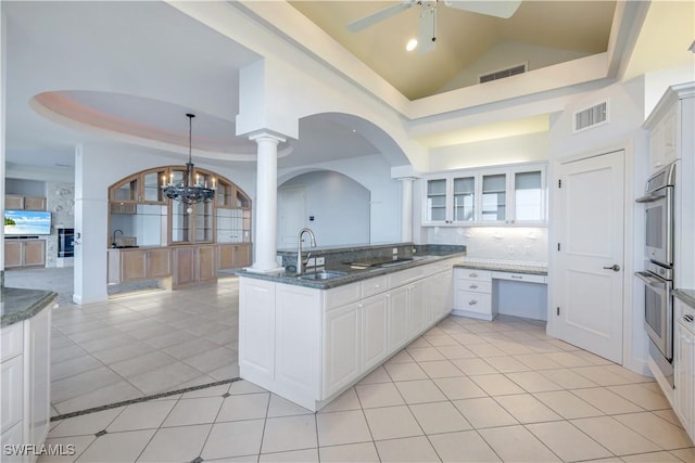 kitchen with visible vents, dark stone counters, glass insert cabinets, a tray ceiling, and a sink