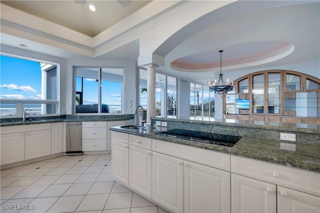 kitchen with light tile patterned floors, dark stone counters, a tray ceiling, black electric cooktop, and a sink