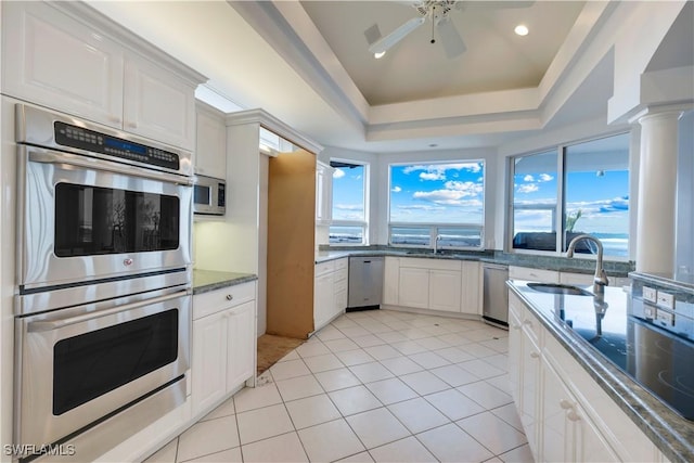 kitchen with light tile patterned floors, white cabinets, a raised ceiling, stainless steel appliances, and a sink