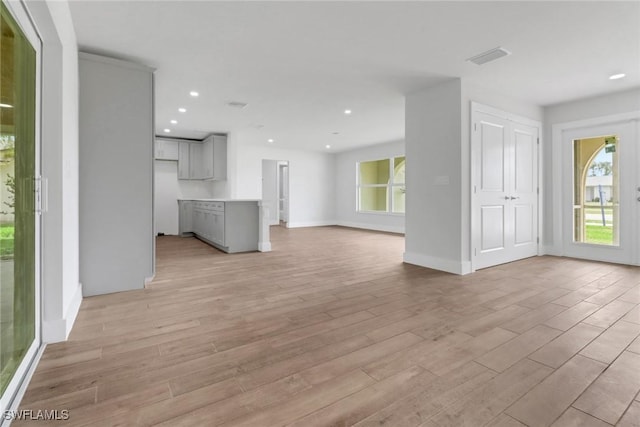 unfurnished living room featuring light wood-type flooring, a healthy amount of sunlight, baseboards, and recessed lighting