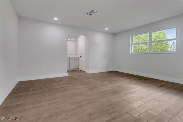 unfurnished room with baseboards, visible vents, arched walkways, wood finished floors, and recessed lighting