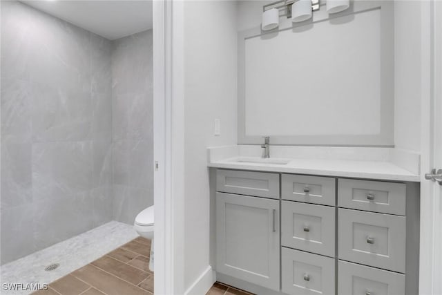 full bathroom with tiled shower, vanity, toilet, and wood tiled floor