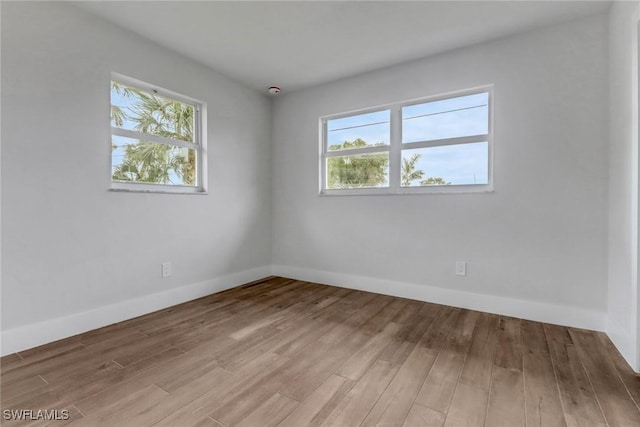 empty room featuring a healthy amount of sunlight, baseboards, and wood finished floors